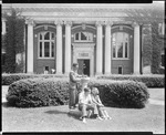 Three Students On Grassy Mall Outside, One Checks Sundial, Large Building Behind At Bates College by George French