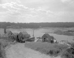 A Row Of Lobster Shacks Along Shoreline, Truck And Boats, Shore Of Inlet Visible On Other Side At Basin Cove by George French