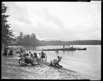 Group Sits In Chairs On Beach, Dock, Boats Afar by George French