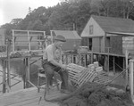 Lobster Fisherman Mending Seine Net, Other Nets Drying On Racks In Background, Old Style Wooden Bait Bags On Pile Of Traps Nearby In New Harbor by George French