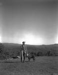 Hunter And His Dog Standing In A Field With Nice View Of The Mountains by French George