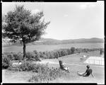 Young Couple Sitting On A Hill Overlooking A Tennis Court With Lake In Background In Canton by French George