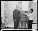 Man And Woman Standing Beside A Sign Advertising Ski Instruction At Riccar Inn by George W. French