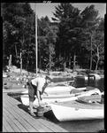 Sailboats Tied Up At Dock, Man Pick Up Bait Can On Kezar Lake by George French