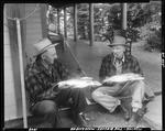 Two Men, Holding Fish They Caught, Sitting On Porch Talking At Moosehead by George French