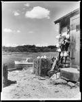 Side Of Fisherman's Shop With Buoys Hung Out To Dry, Boat At Anchor In Harbor by George W. French