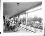 People Relaxing On Porch Of Large Hotel by George French