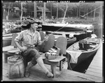 Man Sitting In Chair On Dock Looking Over Contents Of Tackle Box At Brown's Camps by George French