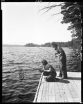 Two Ladies On A Pier Fishing On Long Lake, One Netting A Fish by George French