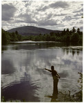 Man Flyfishing A Stream With Green Mountain In Distance by George French