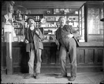 Two Men Leaning Against A Counter In A General Store by George French