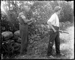 Two Men Holding Long Guns And Standing By A Stone Wall by George French