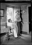Woman In Rocking Chair Mends A Man's Pants While He Stands And Smokes A Pipe by George French
