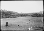 Two Men Playing Baseball In A Field While Two Children Watch by George French
