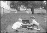 Young Boy And A Baby Playing With Toys On A Blanket On A Lawn by George French