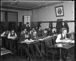 Male College Students In Classroom Studying While Teacher Looks On by George French